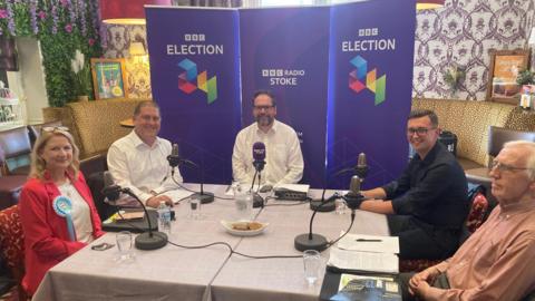 Candidates at the ý Radio Stoke debate sitting around a table with microphones in front of promotional banners