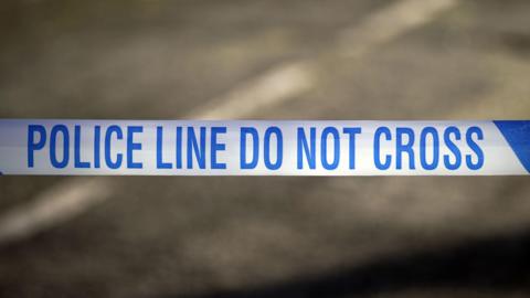 A blue-and-white police cordon stretched across a road, with the words, "police line do not cross".