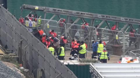 Migrants who have crossed the English Channel in small boats wearing life jackets and being disembarked at the port of Dover.