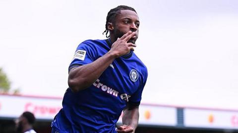 Rochdale's Devante Rodney celebrating scoring by kissing his index finger while wheeling away.
