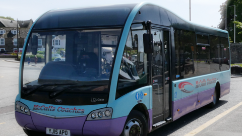 A McCalls Coaches bus which has a purple stripe round the bottom and a lighter blue stripe above that