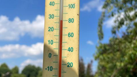 A mercury thermometer reading 27 Celsius in front of a blue sky background