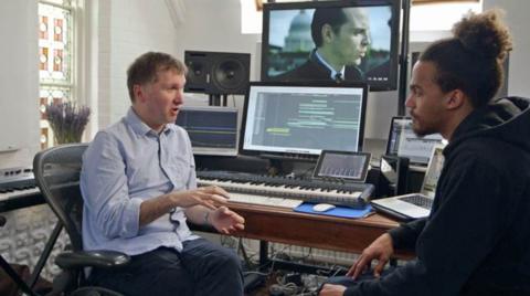 Presenter Dev Griffin sat in a recording studio talking with a music producer. 