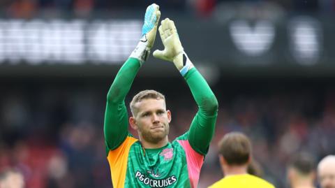 Goalkeeper Daniel Peretz wearing a green goalkeeping shirt, applauds the fans at the end of a game while playing for Southampton.