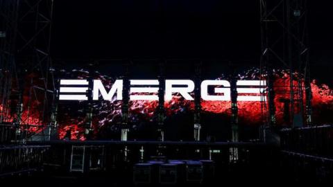 The graphics screen on the stage at the Emerge event spells out the word 'Emerge' in white block letters with a red liquid effect behind it. 