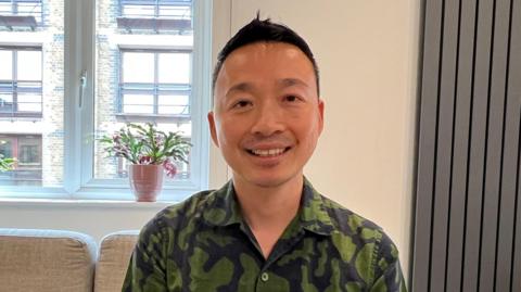 David Ly, a man with short dark hair wearing a green shirt and sitting in front of red flowers