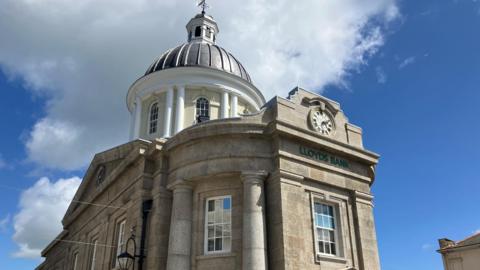 The exterior of the building under a blue sky with a cloud. The dome is visible at the top