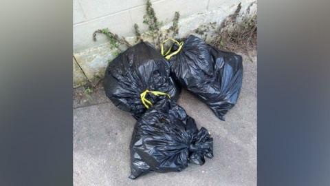 A close-up of three black refuse bags dumped on a pavement