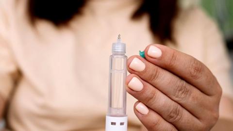 A woman in a peach top and with peach-coloured nail polish holds a weight loss drug syringe