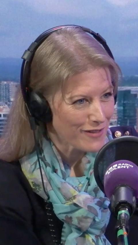 Donna Jones sits in the BBC Radio Solent studio with a backdrop of Southampton behind her. She has long blonde hair with headphones on and a navy blue knit jumper and silk floral scarf round her neck.
