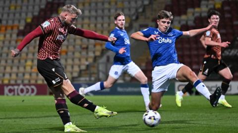 Stephen Humphrys shooting to score Bradford's second goal. He has short light hair and is wearing Bradford's dark red and orange striped kit.