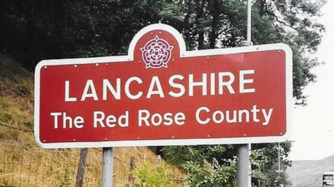 Generic shot of a Lancashire road sign, in red with white lettering saying Lancashire, The Red Rose County