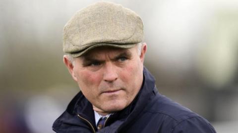 Evan Williams wearing a flat cap. He has short white hair and is wearing a navy jacket. 