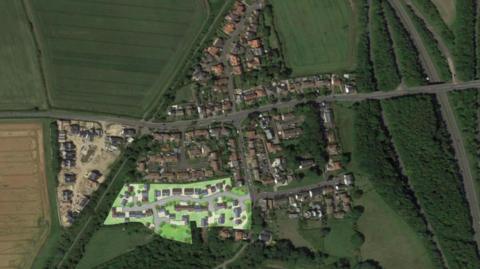 Aerial artist's impression showing where the proposed homes would sit in relation to existing properties. The village is surrounded by fields with some roads cutting through.