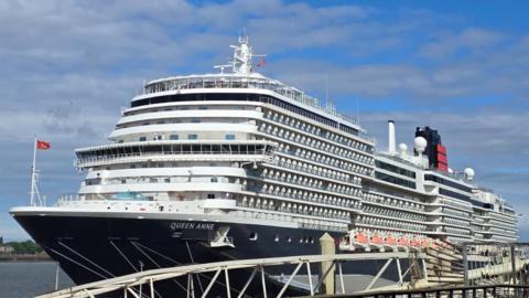 The Queen Anne Cunard cruise ship docked at Liverpool's waterfront. It is a huge white and black vessel with about 10 levels.