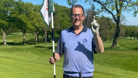 A man stands on a golf course with a pole in his 
