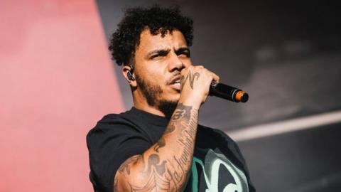 AJ Tracey performing at Laneway festival, he is wearing a black t-shirt and holding a microphone