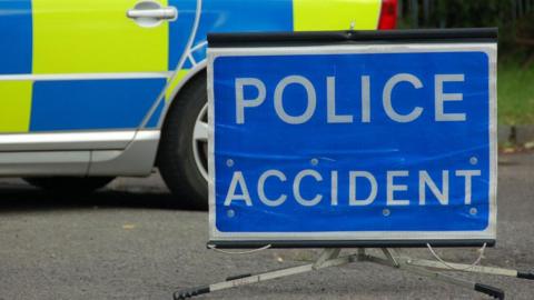 Blue Police accident sign with white writing in front of a police car. Only part of the police car can be seen