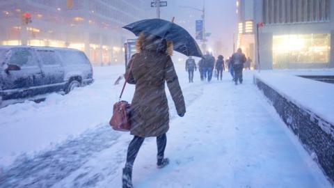A person walks into the snow with an umbrella and their back to the camera on a snowy street in the United States.