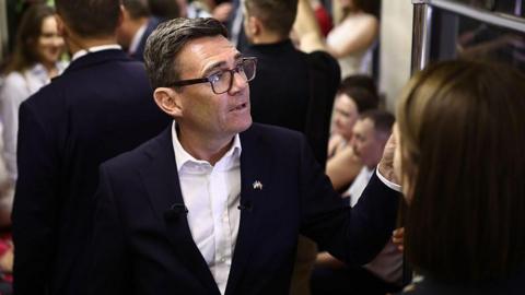Andy Burnham reacts as he stands in a metro carriage among passengers during the journey between the metro stations Zoloti Vorota and Lukanivska on August 24, 2026 in Kyiv, Ukraine.