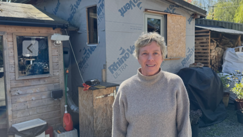 Jane Coyle, a woman in her 60s, is standing in front of a shed made of chipboard