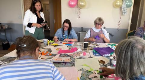 Four women sat around a table doing arts and crafts with brightly coloured paper