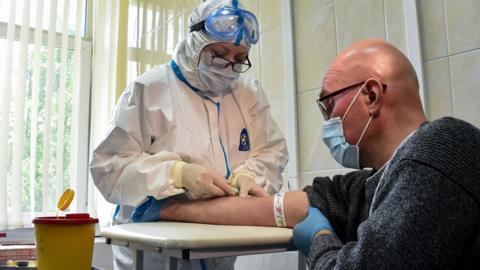 A nurse wearing protective equipment draws blood to test for COVID-19 antibodies at a clinic in Moscow