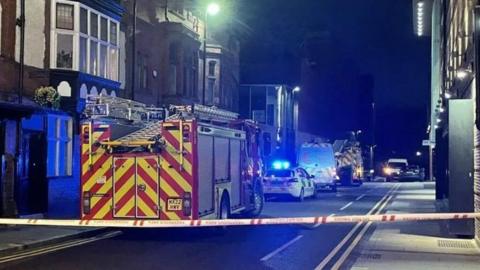 Two fire engines, police cars and a Cadent van can be seen behind a police cordon, close to the scene of the explosion.