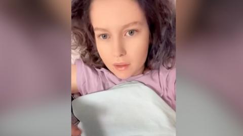 A young woman wearing a pink top lying down in bed