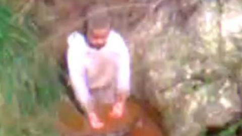 Aerial shot from police helicopter of AJ kneeling in a riverbed