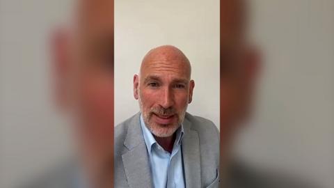 Dan Roan is wearing a light grey suit with a light blue shirt