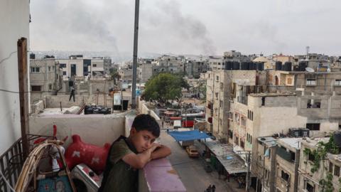 A boy stands on a balcony with a view of billowing smoke due to renewed Israeli strikes in Rafah city in the southern Gaza Strip on May 28, 2024
