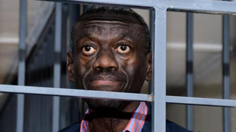 Ugandan opposition politician Kizza Besigye, staring ahead stands in dock behind bars at the Uganda Military General Court Martial in Kampala