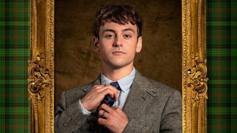 The image shows Tom Daley in a formal suit and tie, adjusting his tie. He is framed by an ornate golden frame with green tartan-patterned sides. The background features a textured brown surface.
