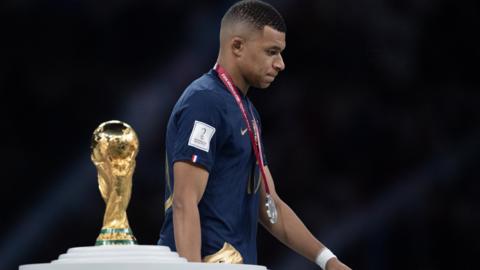 Kylian Mbappe walks past the World Cup trophy