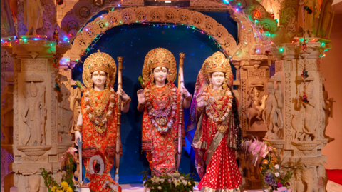 Three statues at the Shree Sanatan Hindu Mandir on December 9,2015 in London, England. They are posed next to each other wearing red silks and garlands round their necks and stood on a highly decorative dais.