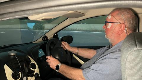 A man with sensors attached to his head driving a car simulation