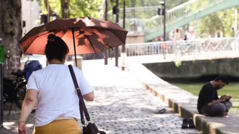 Woman walks in Paris with umbrella to shield sun