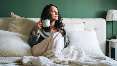 A woman in bed drinking a cup of tea