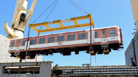 A railway carriage being unloaded onto the track by a crane