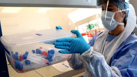 A laboratory technician wearing full PPE (personal protective equipment) holds a container of test tubes containing live samples taken from people tested for the novel coronavirus, at a new Lighthouse Lab facility dedicated to the testing for COVID-19, at Queen Elizabeth University Hospital in Glasgow on 22 April 2020.