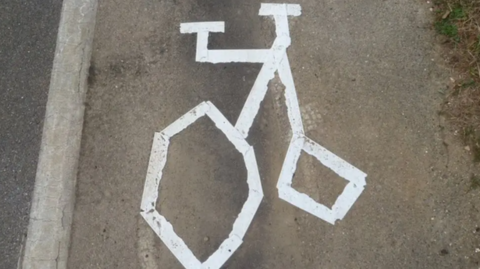A strange-looking line-drawing of a bicycle painted in white paint on a road