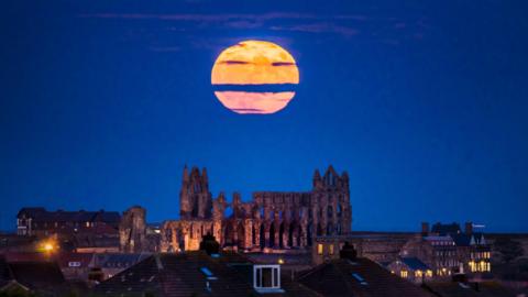 A large full Moon rises above Whitby Abbey with mainly clear skies and just a little cloud covering the Moon.