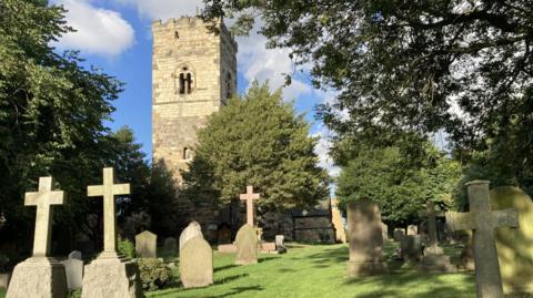 The picturesque village church can be seen in glorious sunlight over rows of headstones. 