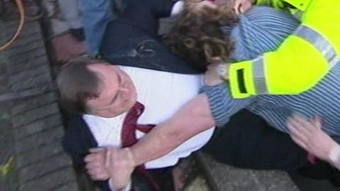 John Prescott is pushed back against a wall by a protester; there is egg on Prescott's shoulder