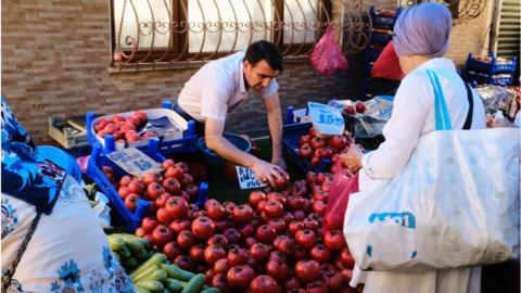 Fruit seller in Turkey with woman buying in foreground.