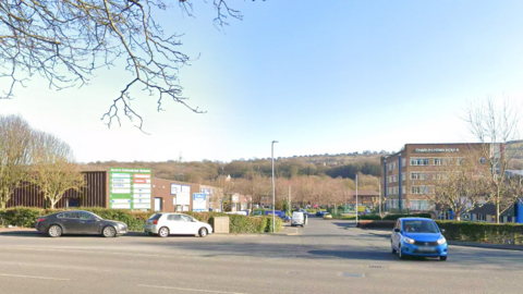 Street View image showing the entrance to the Acorn Industrial Estate in Baildon, with a blue car leaving the junction and black and white cars turning in.