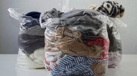 Three plastic bags stuffed with clothes placed on a table against a white background