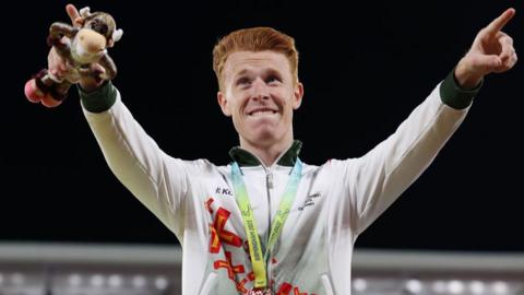 Alastair Chalmers points his arms while on the podium at the 2022 Commonwealth Games