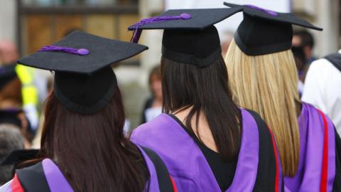 The backs of three women wearing black gowns and graduation hats with purple sashes.